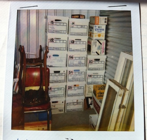 A polaroid of my very organized storage unit with labels on the boxes corresponding to an elaborate notebook detailing contents of each – note the stacked up windows rescued from dumpsters and construction sites.