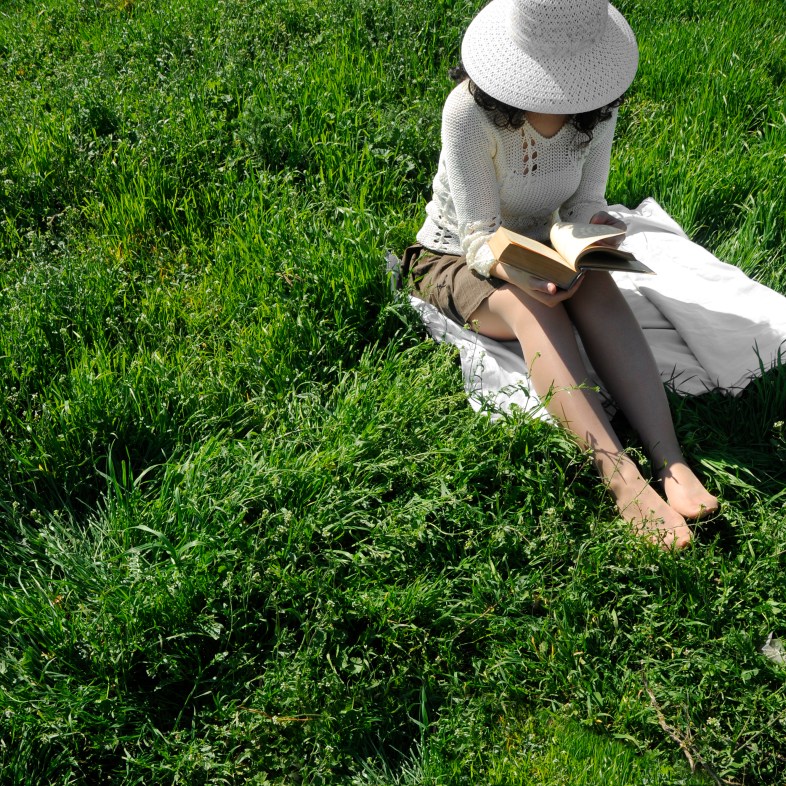 Young woman sitting in the grass, reading a book