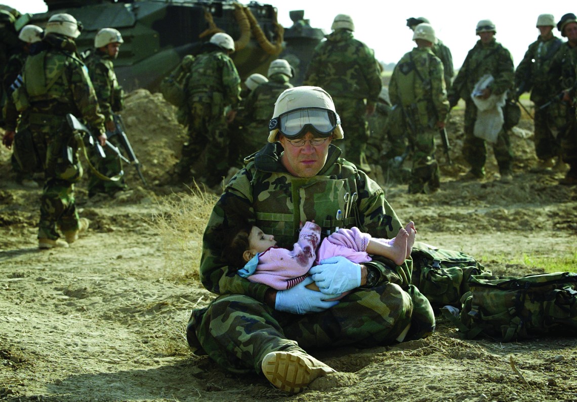 U.S. Navy Hospital Corpsman HM1 Richard Barnett, assigned to the 1st Marine Division, holds an Iraqi child in central Iraq in this March 29, 2003 file photo. Confused front line crossfire ripped apart an Iraqi family after local soldiers appeared to force civilians towards positions held by U.S. Marines. March 20 marks the one year anniversary of the beginning of the U.S. led war against Iraq. The war started on March 20 Baghdad local time, March 19 Washington D.C. local time. REUTERS/Damir Sagolj HIGHEST QUALITY AVAILABLE - RTR1ADKJ