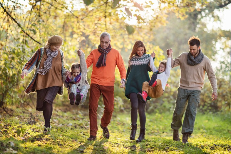 Playful multi-generation family having fun during autumn day in nature while holding hands and swinging small kids.