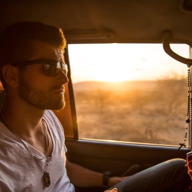 Handsome man riding in car, sunset behind him.