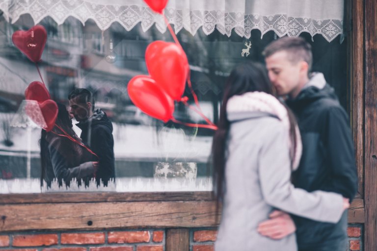 Couple kissing in front of window heart balloons