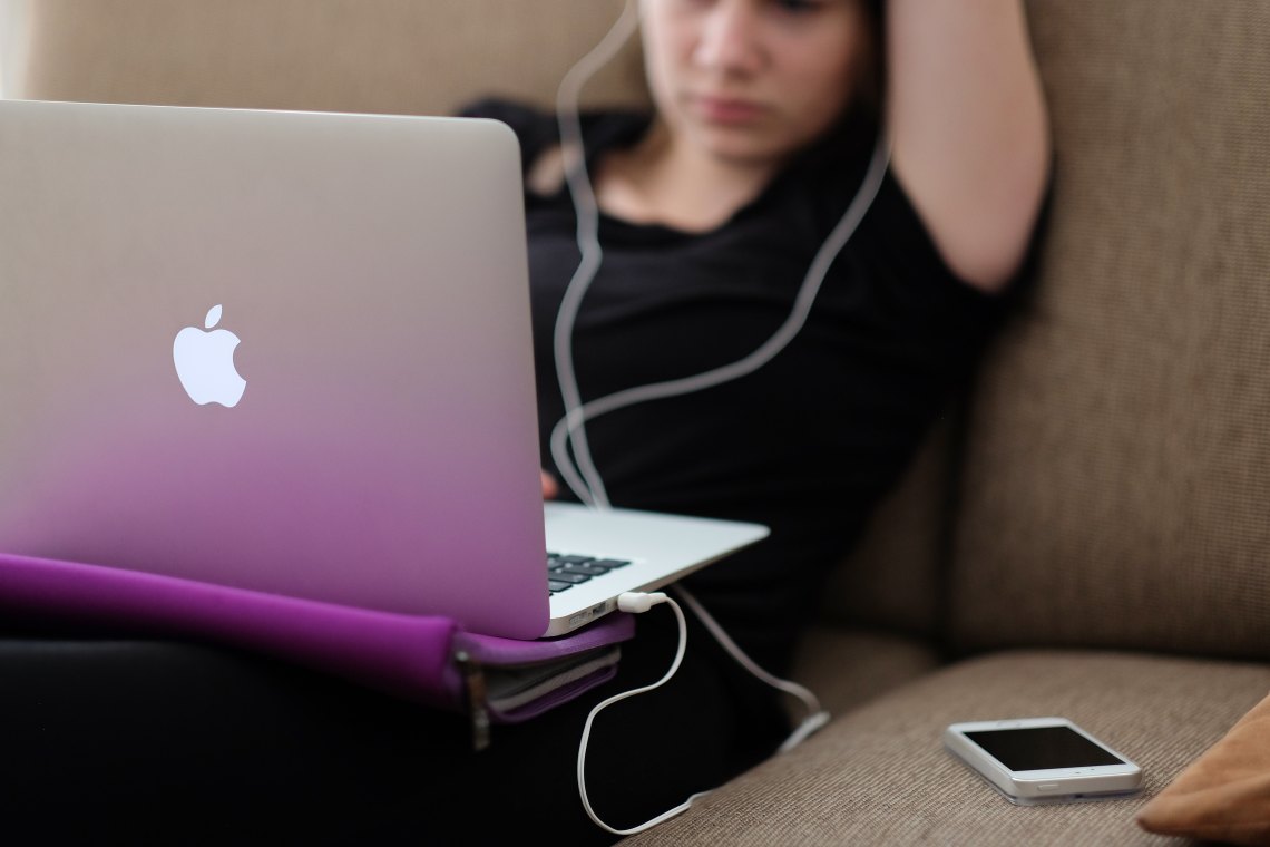 A feel listening to her iPhone while playing on her computer