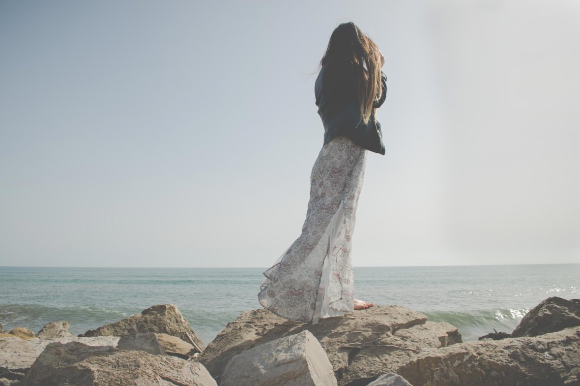 Woman in long skirt standing on beach rocks