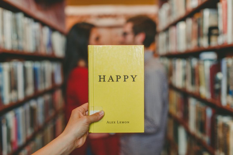 someone holds up a book that says "happy" in a library