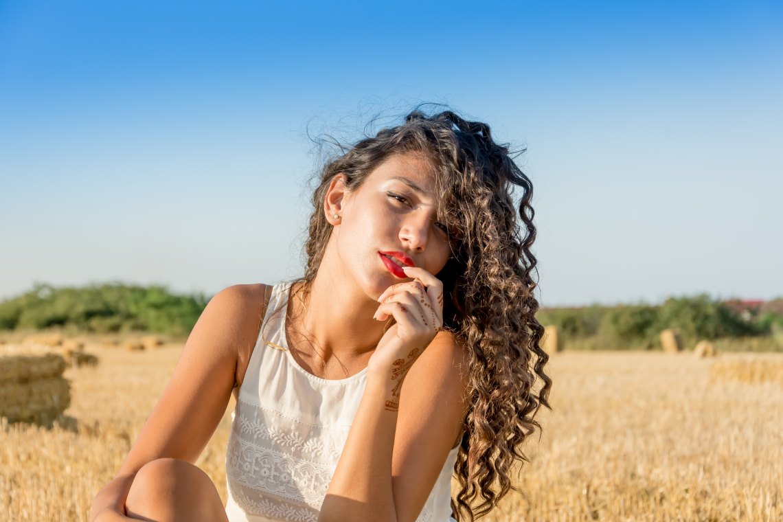 Girl with dark curly hair red lipstick in field