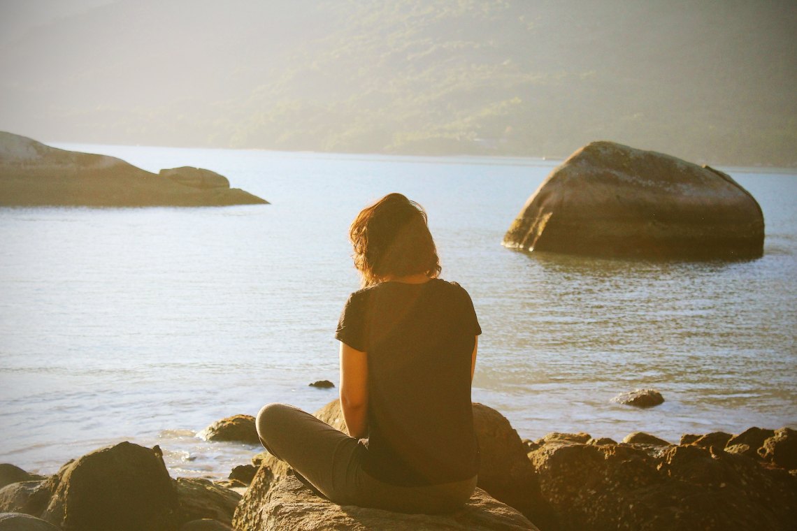 Woman sitting on rocks looking at beach
