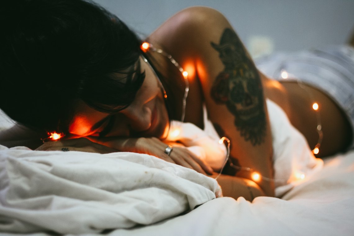 a girl in a bed with some lights and tattoos