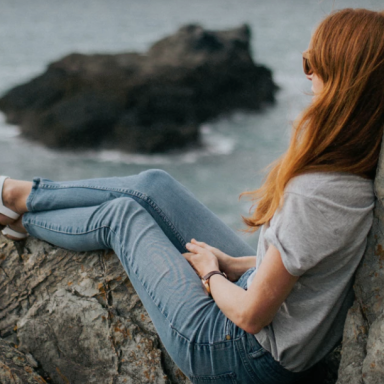 Girl sitting on rocks by ocean