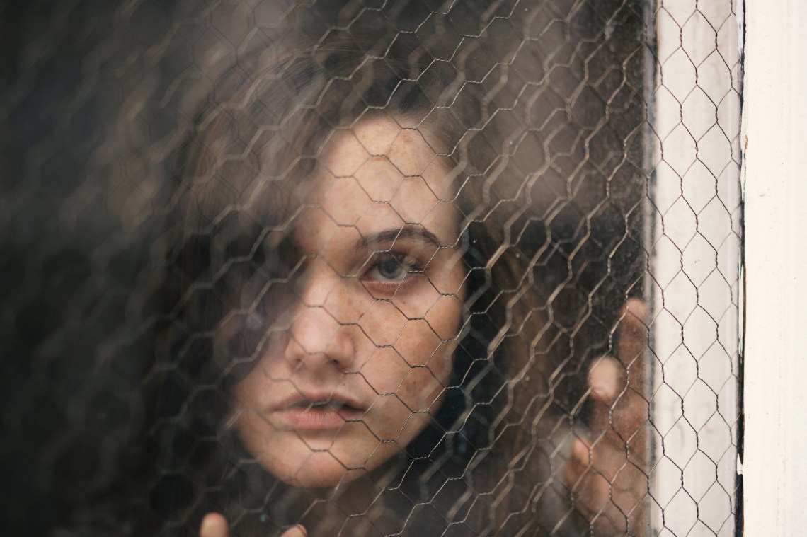 Woman stares out from behind a wire fence, looking isolated