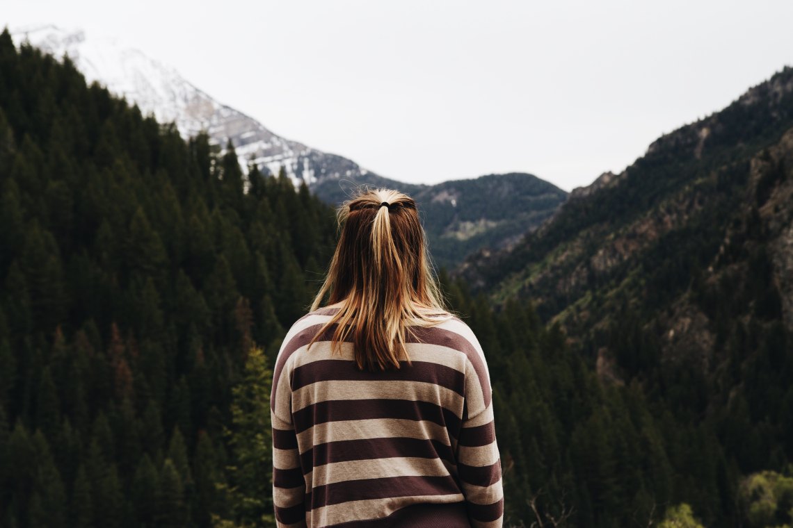 A young woman looks off into the mountains, her back to the camera