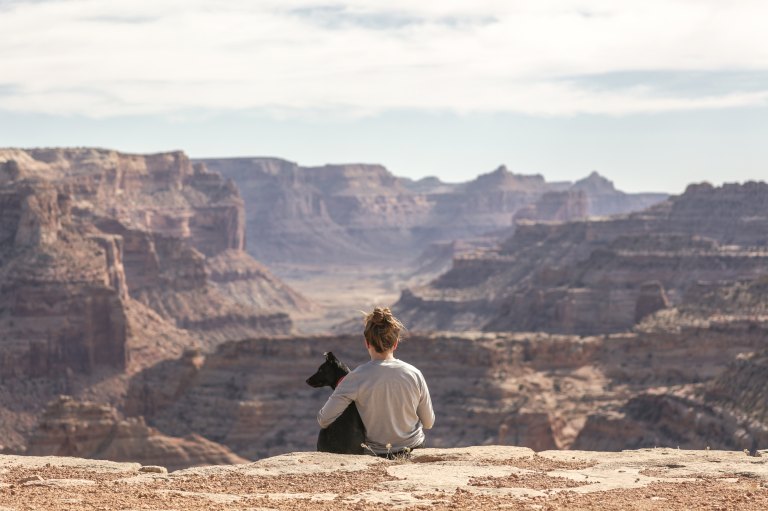 Woman and dog sitting in front of canyon