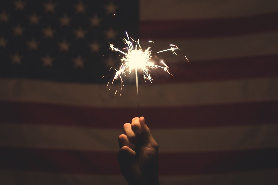 Someone holds a sparkler in front of the American flag