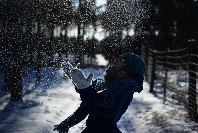 A girl bundled up in winter clothes happily plays with snow while standing on a snowy path