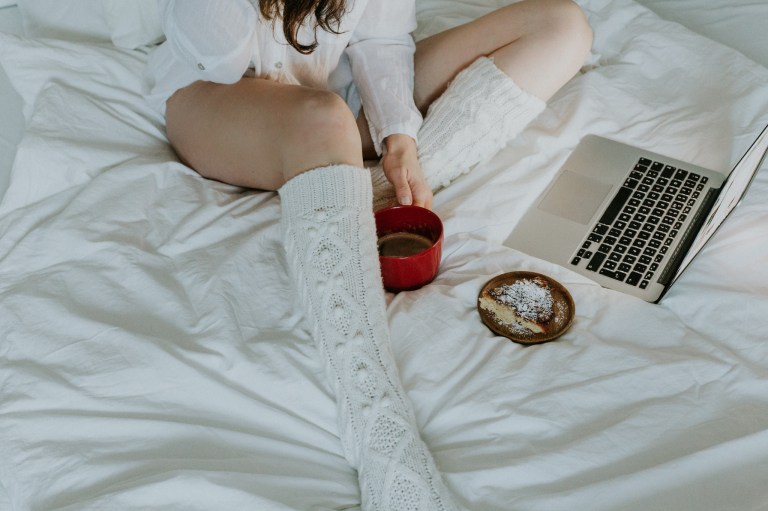 legs and coffee and macbook on white sheets