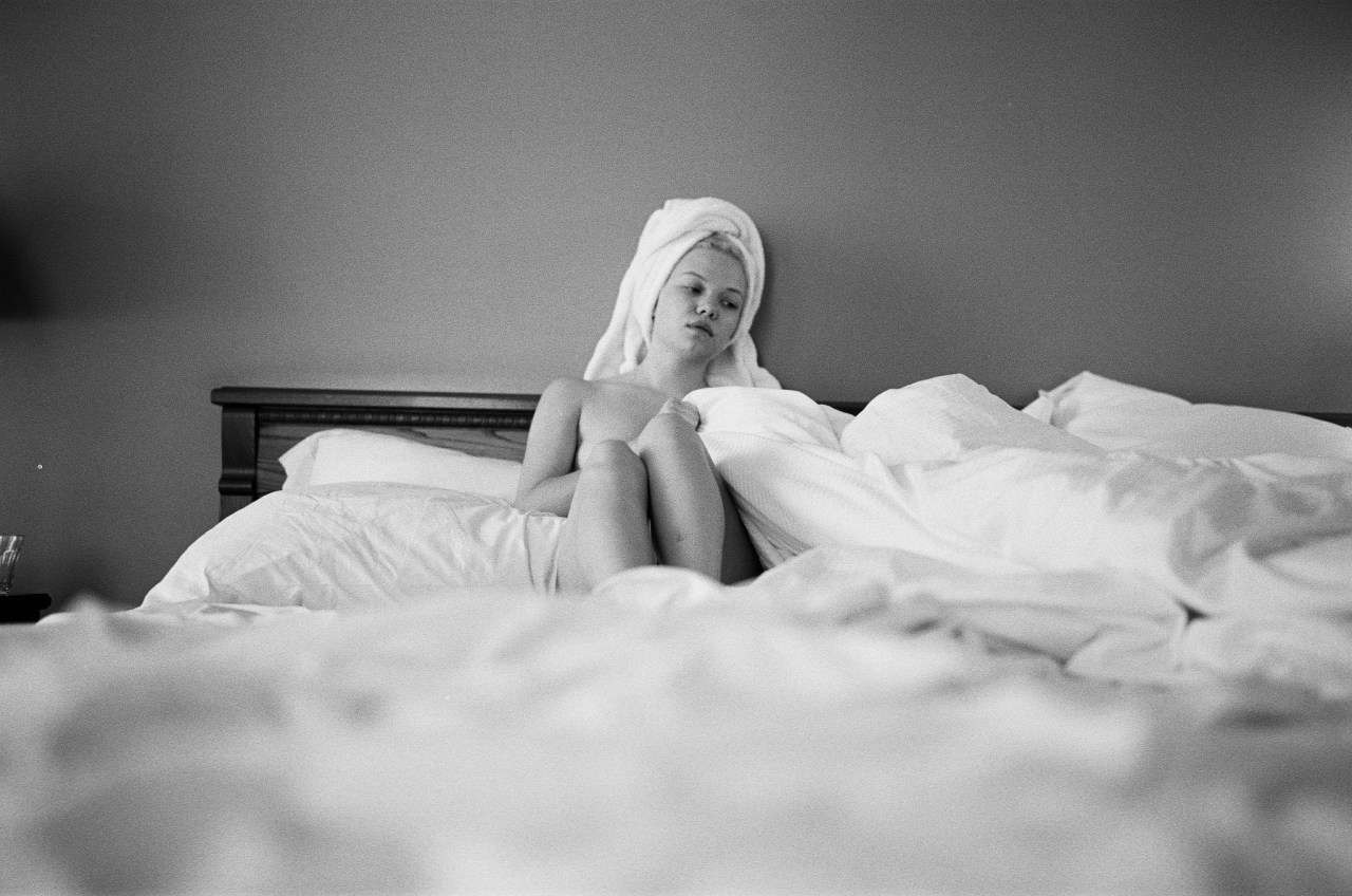 A woman sits in bed half-naked while being surrounded by blankets