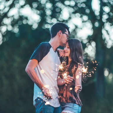 A man and a woman holding sparklers as the man kissing the woman's forehead
