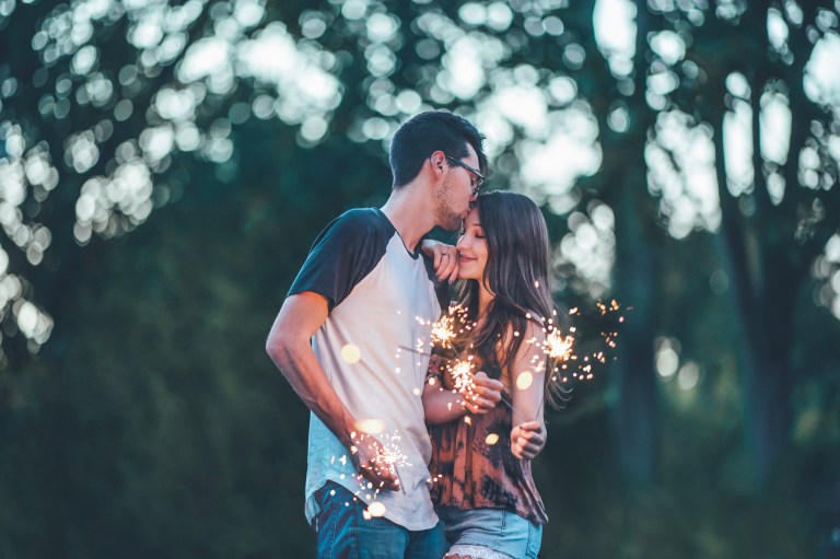 A man and a woman holding sparklers as the man kissing the woman's forehead