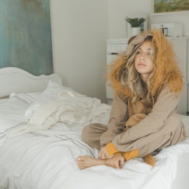 girl in lion onesie sitting on bed