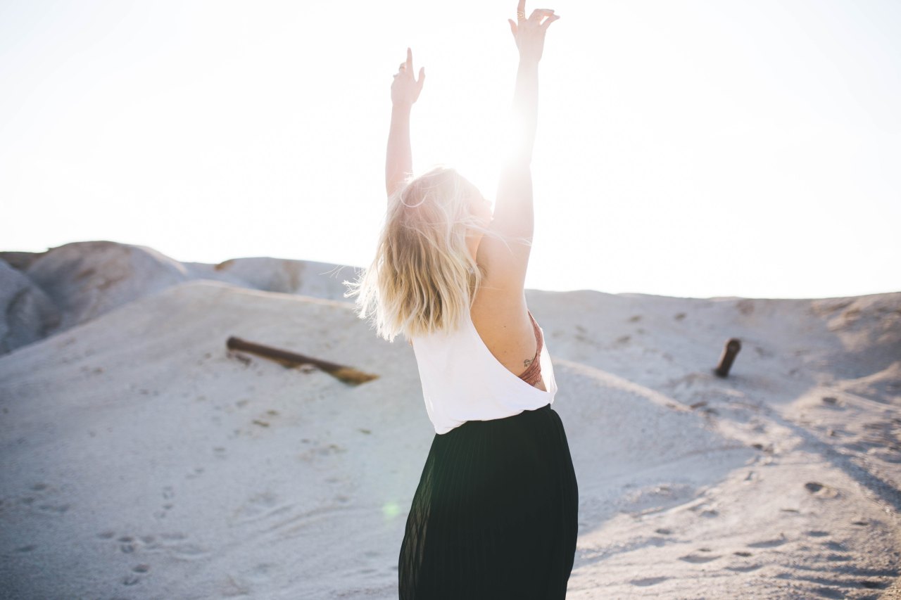 Woman walks in the sand and throws her hands up into the sun