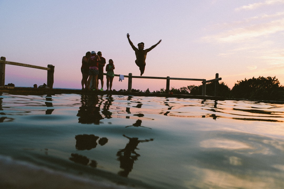 Young person having fun and jumping into the pool while friends watch during sunset.
