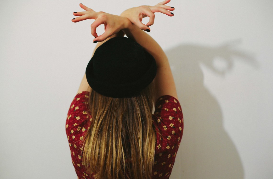 holding her hands about her head while wearing a hat