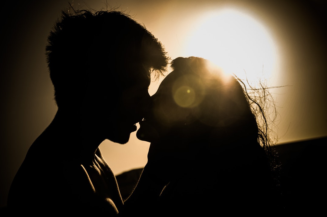 Classic sunset silhouette of couple kissing with sea wind frizzing their hair