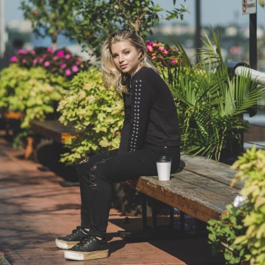 blond woman dressed sitting on a park bench with a paper cup beside her