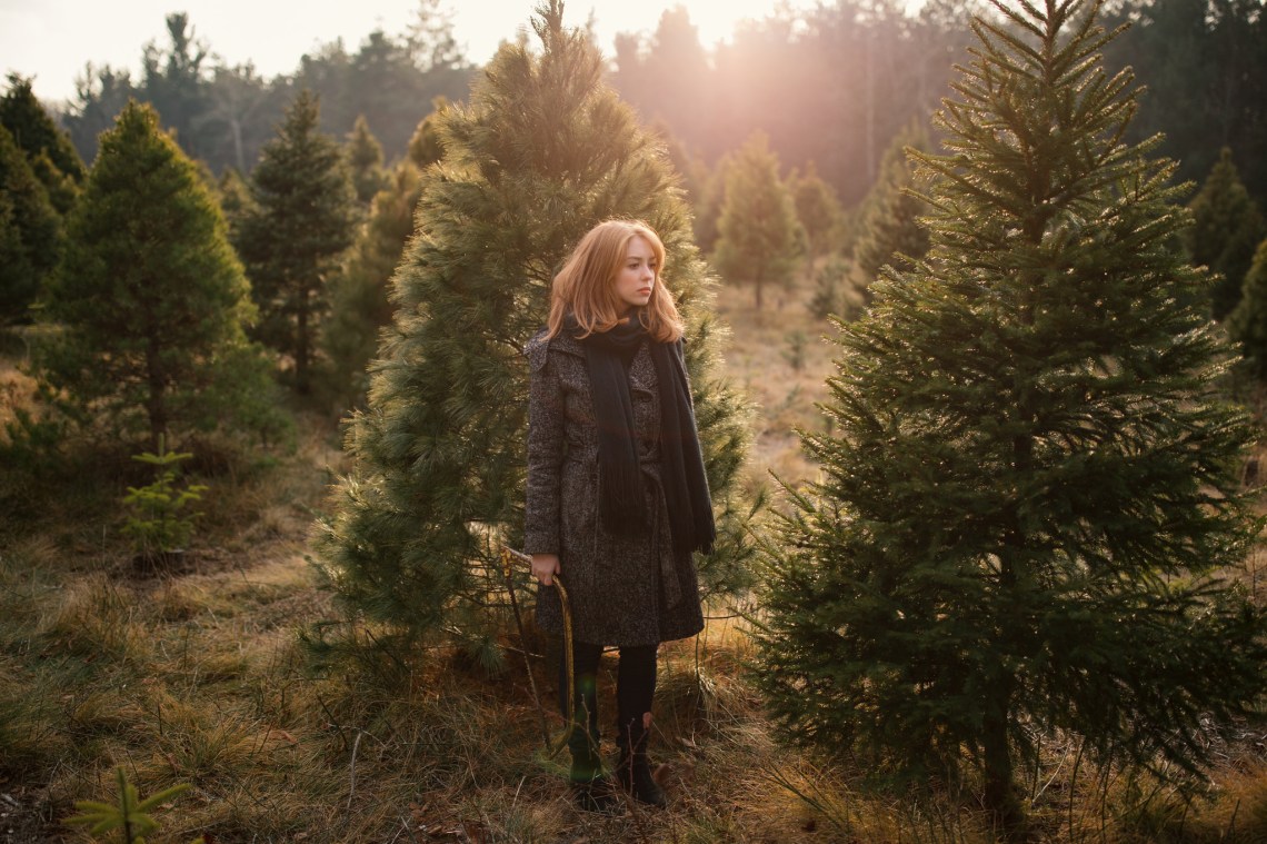 Lady Silently Stands among the Christmas Trees while Holding a Hand Saw