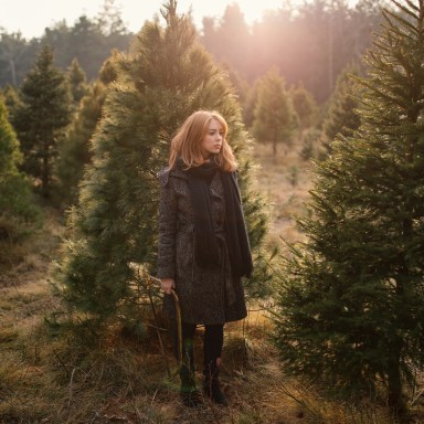 Lady Silently Stands among the Christmas Trees while Holding a Hand Saw