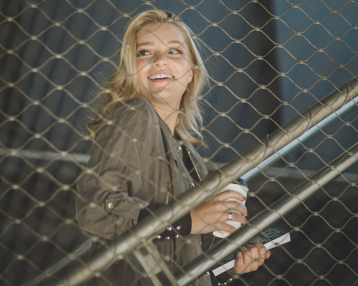 Pretty blonde woman happily going up the stairs holding her paper cup and book