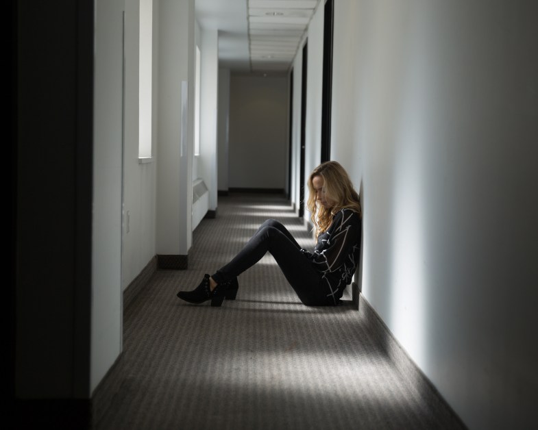 Young woman dressed in black sitting on the floor in a shadowy corridor