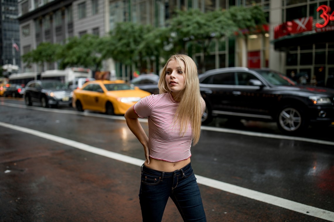 Blonde woman in a striped red shirt looking around while walking along the street in the rain