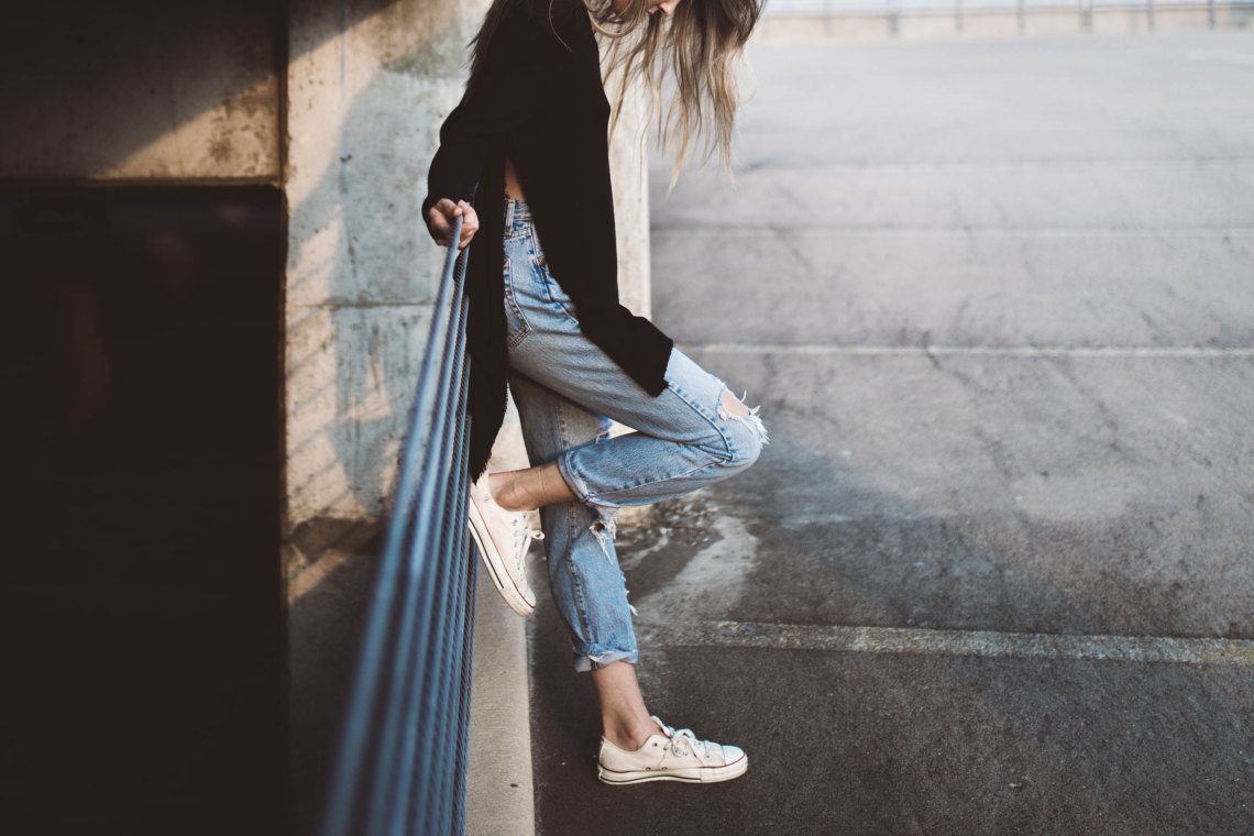 woman leaning against post with ripped jeans