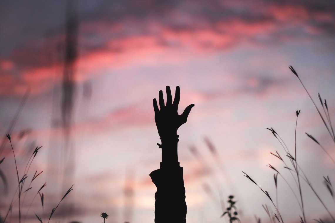 a hand reaching up over a sunrise