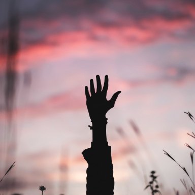 a hand reaching up over a sunrise