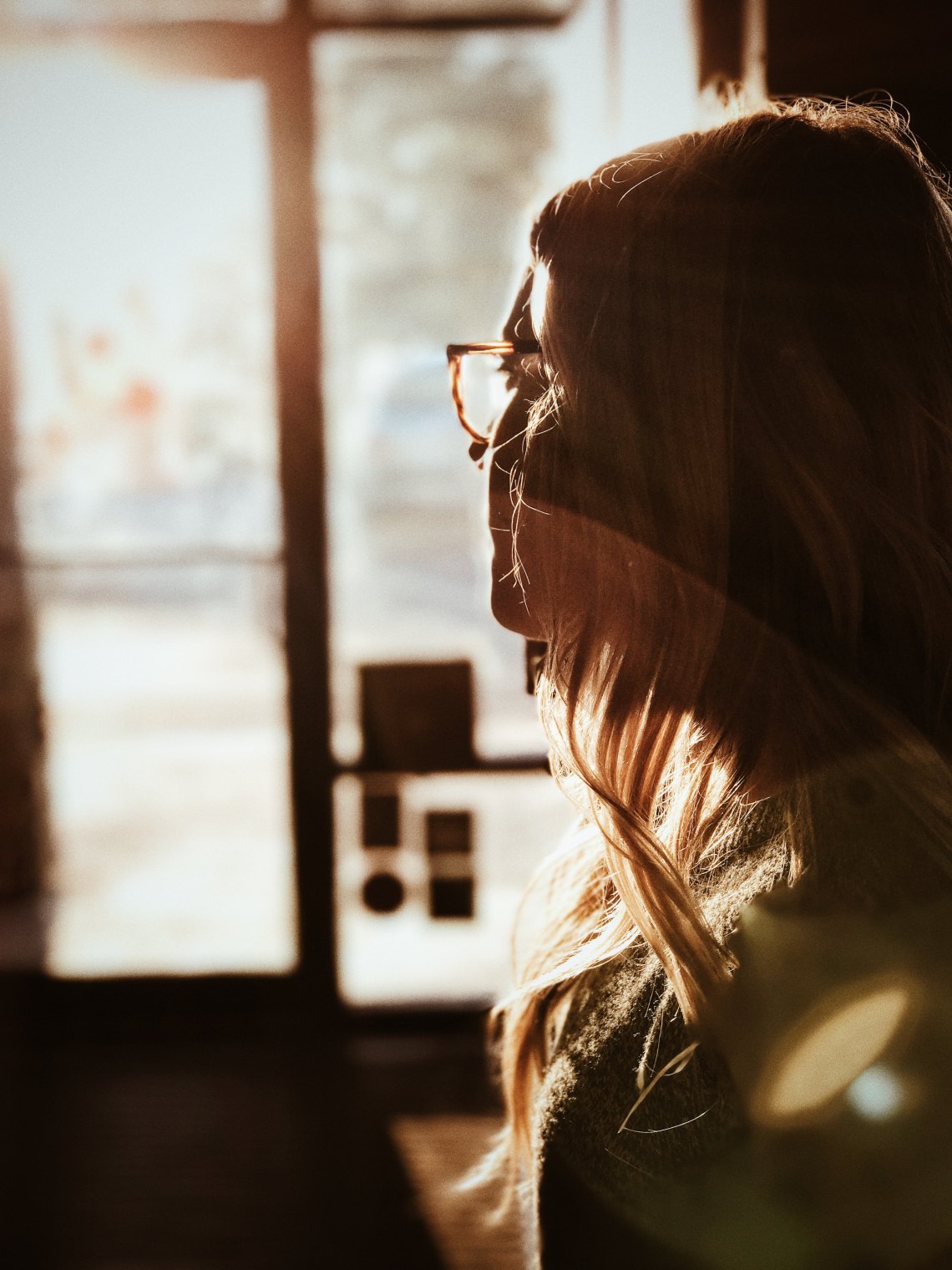 girl in glasses backlit and staring in a window
