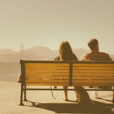 A man and a woman sit on a bench, looking out into the distance, probably about to break up