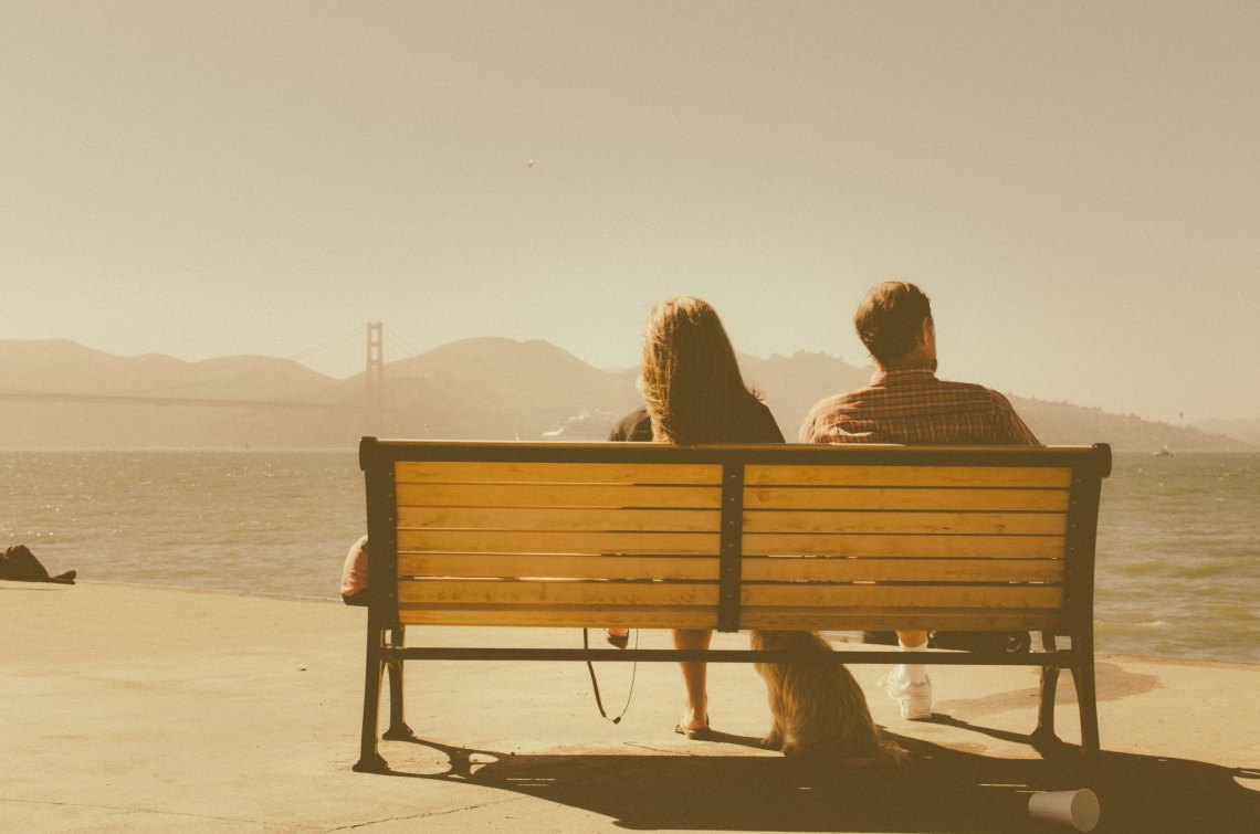 A man and a woman sit on a bench, looking out into the distance, probably about to break up