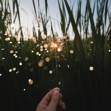 a hand holding up a sparkler in front of grass