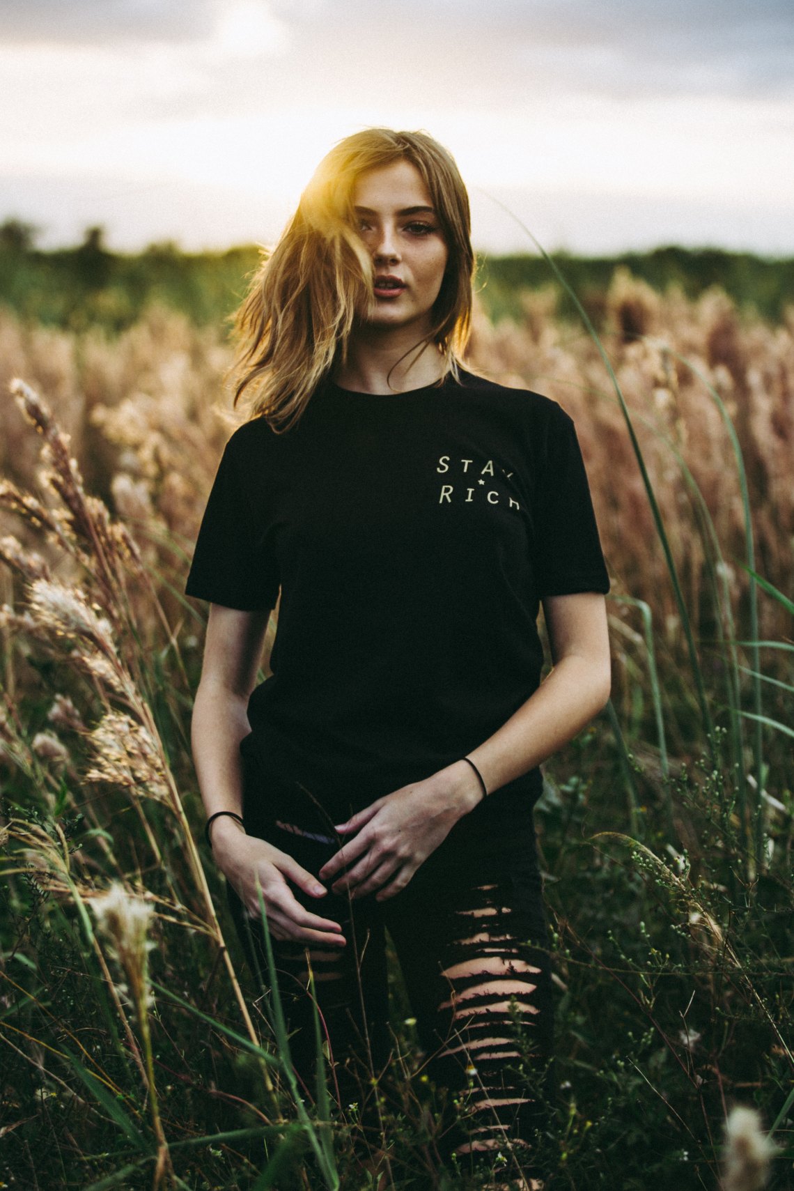 girl standing in a field in a stay rich shirt