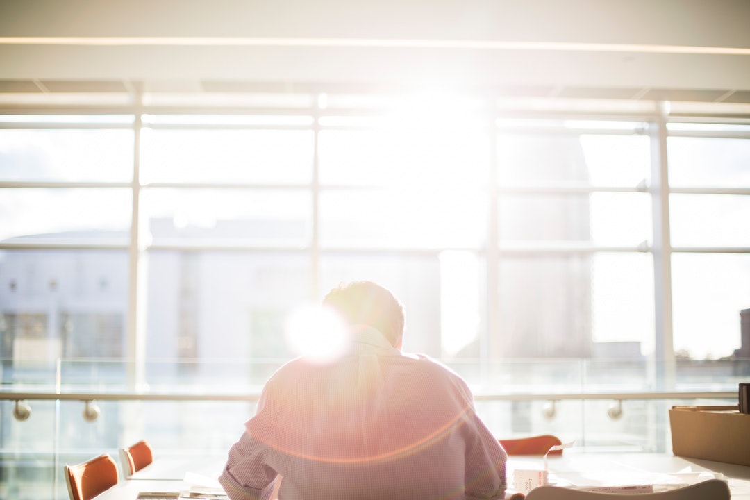 A man reading in an office directly sitting and facing towards the window flooded with rays of sunshine