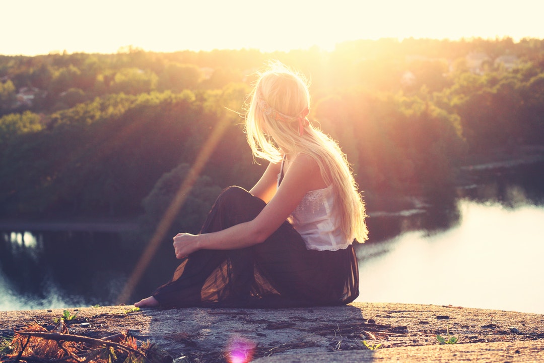 A young blonde woman sitting on rocks overlooking a lake