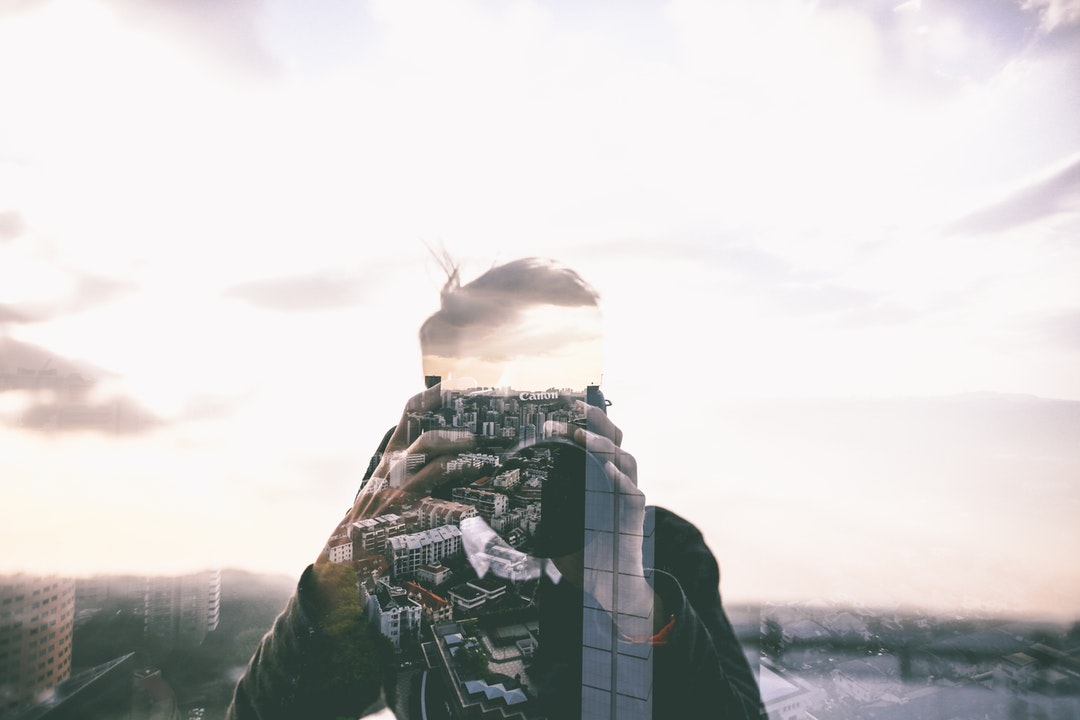 The reflection of the city in a window obscuring the reflection of a photographer with a Canon camera