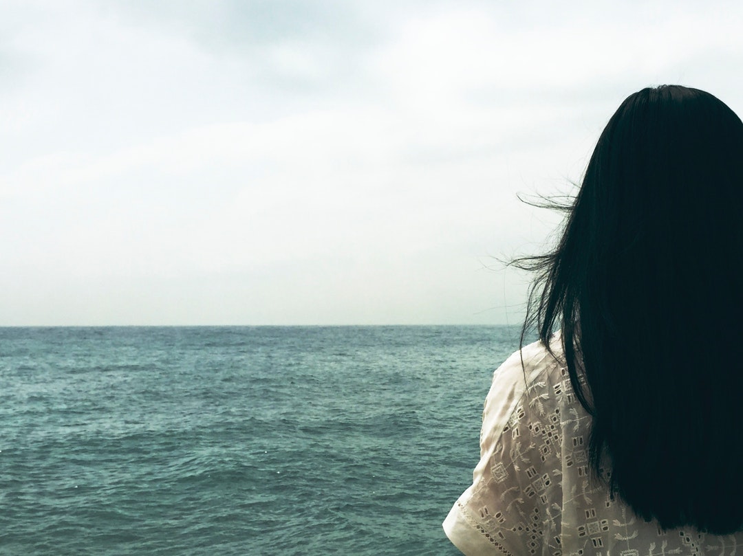 A dark-haired woman looking off into the choppy sea stretching to the horizon
