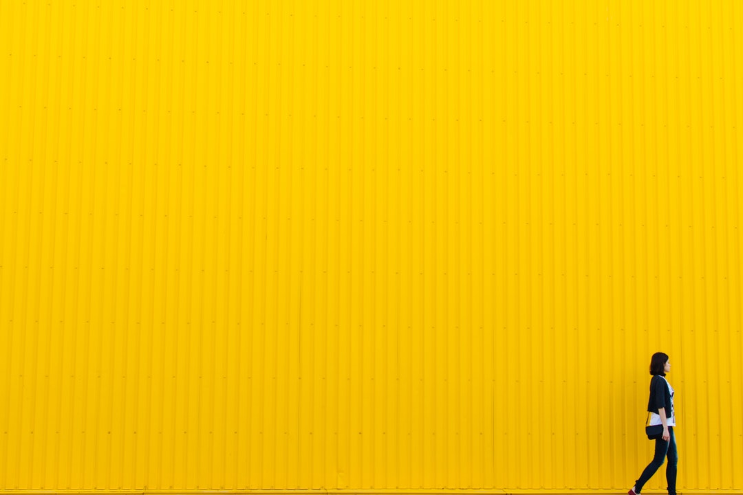 A female walking by a yellow lined texture building wall