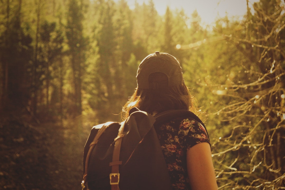 A woman with a backpack looking at a dense forest in front of her