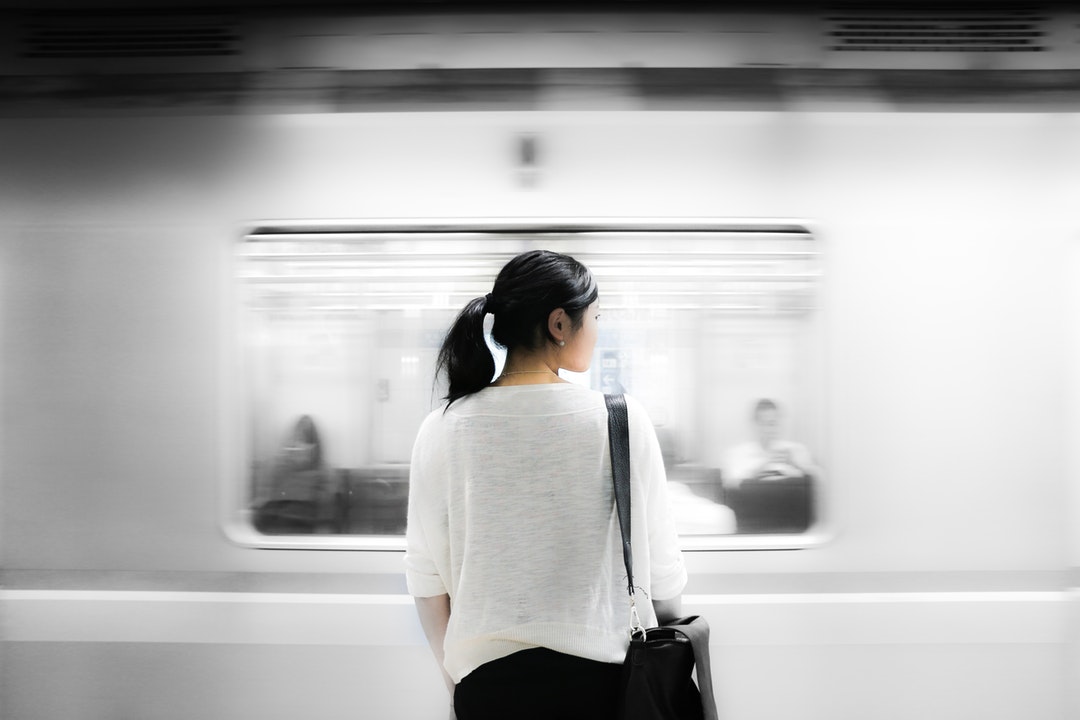A subway train passing in front of a woman with a black leather bag