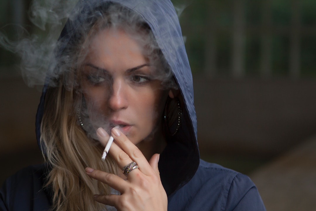 A blonde woman in a blue hoodie smoking a cigarette in Люберцы