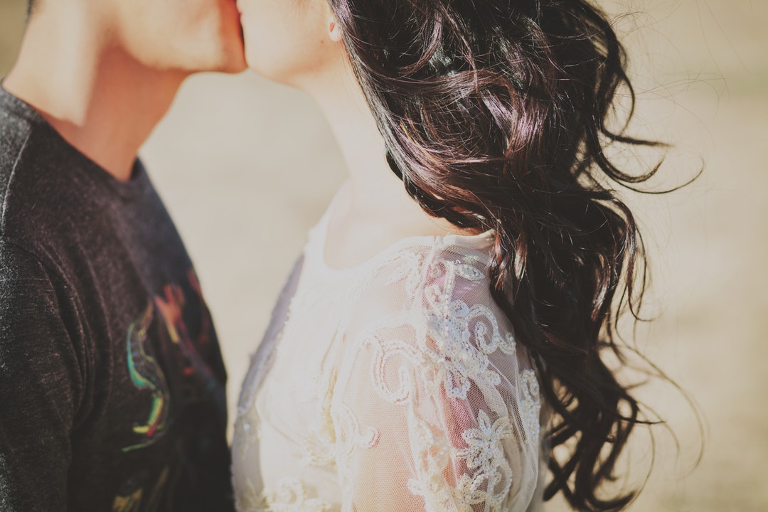 Young woman with lacey dress and hair blowing in wind kisses her boyfriend
